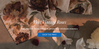 A styled flat-lay of a fabric print featuring large vintage-style floral motifs in brown, burgundy, and cream tones, with overlaid text reading 'Meet Vintage Roses' and a blue 'SHOP THE PRINT' button. 